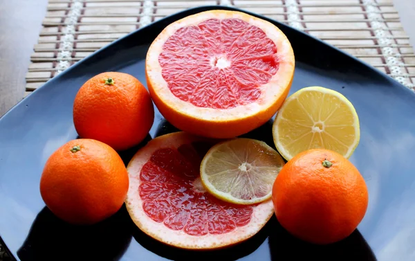 Assorted citrus fruits on black glossy plate — Stock Photo, Image