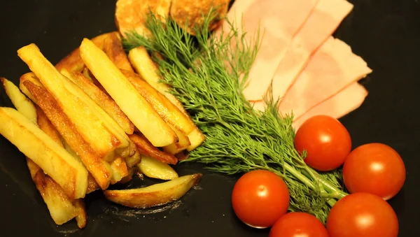 Bratkartoffeln, Schinken in Scheiben, Kirschtomaten und Gemüse auf schwarzem Teller serviert — Stockfoto