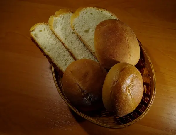 Segmenten van brood en ronde schuifregelaar broodjes in stro graanschuur op houten tafel — Stockfoto