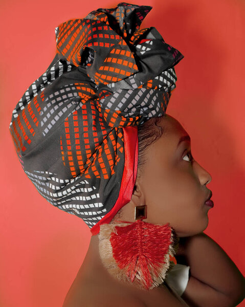 Joven mujer afro / negra posa con turbante y aretes rojos culturales.