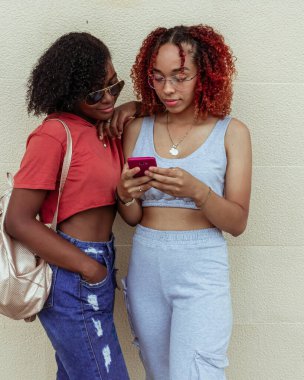 Jovenes amigas afro con lentes revisan el celular
