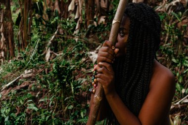 Mujer negra de selva sentada, reposada en su arma mientras piensa