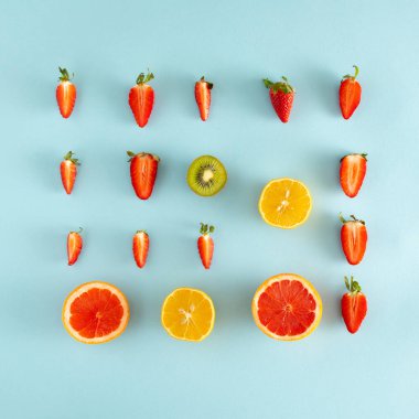 Taze tropikal sarı limon, kırmızı greyfurt ve pastel mavi arka planda yeşil yapraklı taze kırmızı çilek tarafından yapılmış yaz küpü. Matematik şekli. Soyut sanat. yaratıcı fikir.