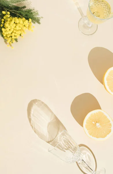 Sarı mimoza ve yeşil yapraklı yaratıcı konsept, iki taze limon ve iki şampanya bardağı, güneşli arka planda gölgeler. Minimum düzlük. en az arkaplan