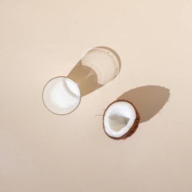 Hindistan cevizinin yarısı bardakta hindistan cevizi sütü ve parlak krema arkaplanı. Asgari yaratıcı dekorasyon yaz fikri