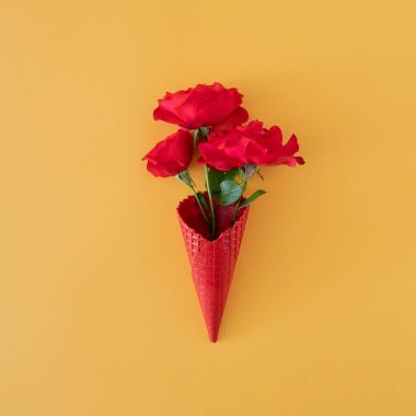 Taze kırmızı güller, yeşil yapraklar ve yaz sarısı arka planda dondurma külahı. En az yaratıcı dekorasyon fikri. en düşük düzlük.