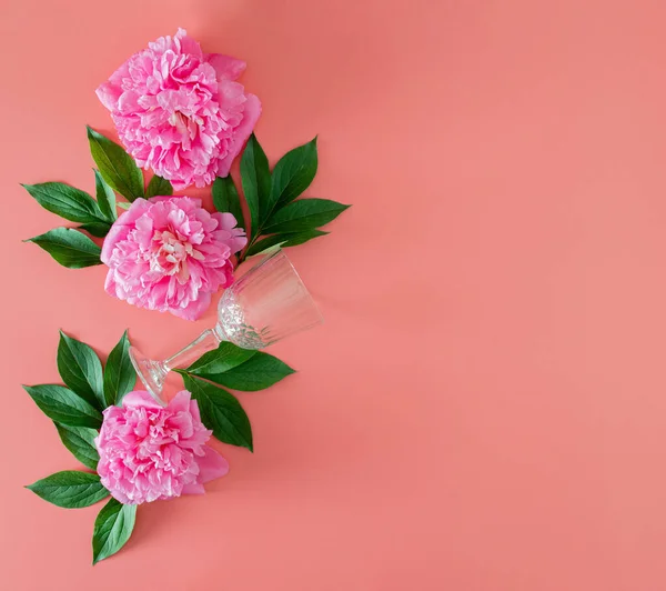 Yeşil yapraklı taze pembe şakayık ve pembe pastel arka planda şarap kadehi fotokopi alanı ile. Kopyalama alanı olan asgari tropikal yaz düzlüğü. en küçük bahçe arkaplanı.