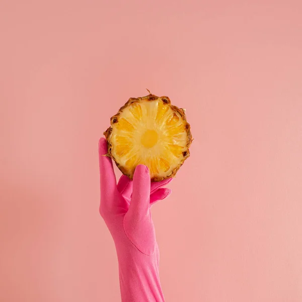 Pembe eldivenli bir el ve pembe güneşli yaz aydınlatma arka planında bir dilim taze ananas. Soyut sanat. asgari arkaplan fikri.