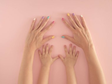 Pastel pembe arka planda renkli tırnakları olan anne ve kızın elleri. yaz modern tropikal soyut sanat ve kadın eli. asgari modern ebeveynlik fikri.