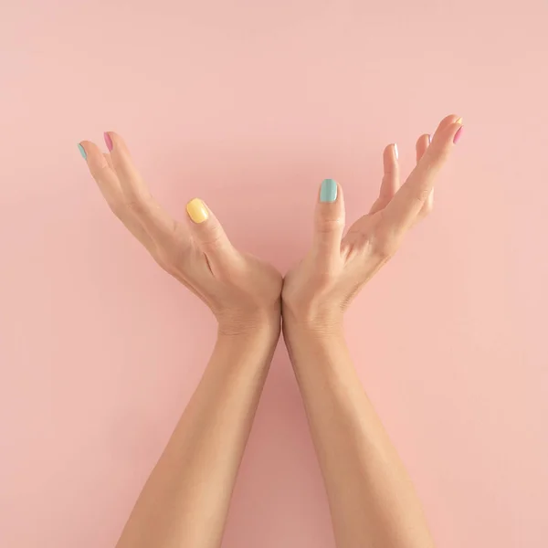 Pastel pembe arka planda renkli tırnakları olan kadın elleri. kopyalama alanı. yaz modern tropikal soyut sanat ve kadın eli. asgari arkaplan fikri.