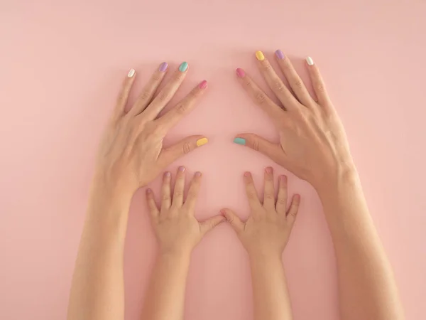 hands of mother and daughter with colorful nails on the pastel pink background. summer modern tropical abstract art with female hand. minimal modern background parenting idea.
