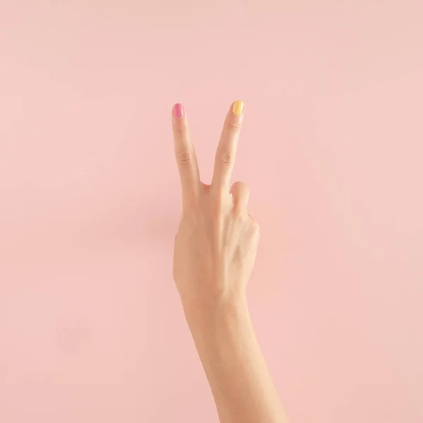 Pastel pembe arka planda renkli tırnakları olan kadın elleri. kopyalama alanı. yaz modern tropikal soyut sanat ve kadın eli. 2 numarali asgari arkaplan fikri