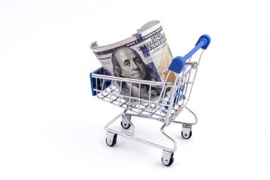 Birkaç yüz Amerikan doları beyaz arka plandaki bir süpermarkette minyatür bir alışveriş arabasında yatıyor.