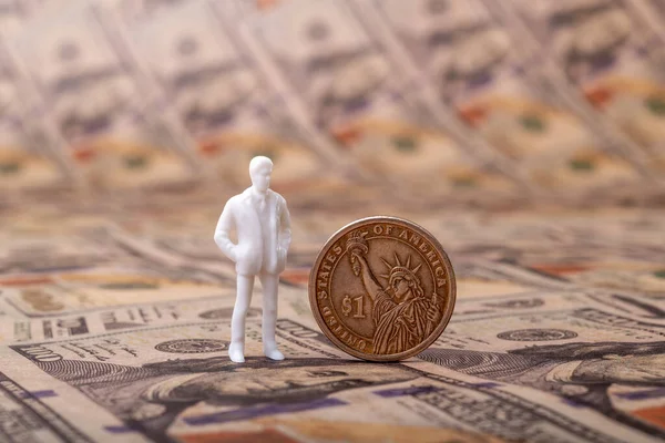 Stock image A plastic figurine of a symbolic person stands next to a 1 American dollar coin against a background of 100 American dollar bills