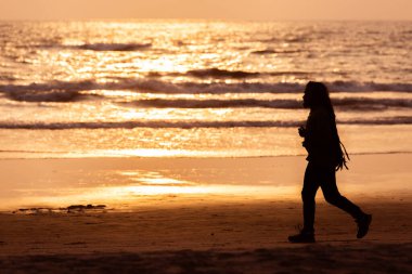 Arambol, Goa, Hindistan, 25.02.2017. Uzun saçlı bir adamın silueti Goa, Arambol köyü sahillerinde koşuyor, akşamleyin Hint Okyanusu kıyısında gün batımında.