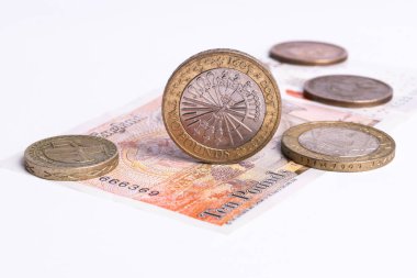 Kenarda duran bir kilo bozuk para, beyaz arka planda duran 10 pound 'luk banknotun arka planında diğer İngiliz paraları.