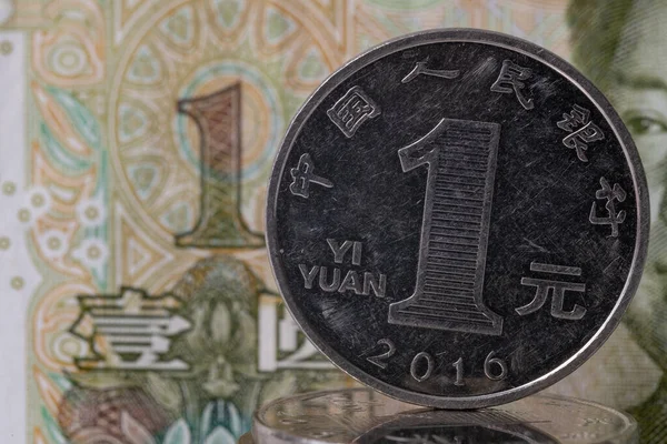 A coin in denomination of one Chinese yuan against the background of a fragment of a one-yuan note