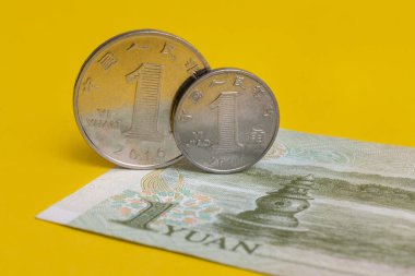 Bir Çin Yuan 'ı ve küçük bir sikke 1 jiao' yu sarı arka planda 1 yuan 'lık banknotun kenarında duruyor.