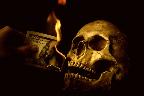 在一个黑色背景的假骷髅旁边 有一个燃烧着的100美元钞票 — 图库照片