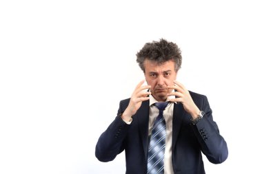 Tıraşsız, orta yaşlı, takım elbiseli, dağınık saçlı ve duygusal bir yüzü olan bir adam beyaz bir arka planda önümüze bakıyor..