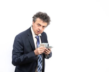 Tıraşsız, orta yaşlı, takım elbiseli, dağınık saçlı ve duygusal yüzlü bir adam beyaz arka planda 100 dolar tutuyor.