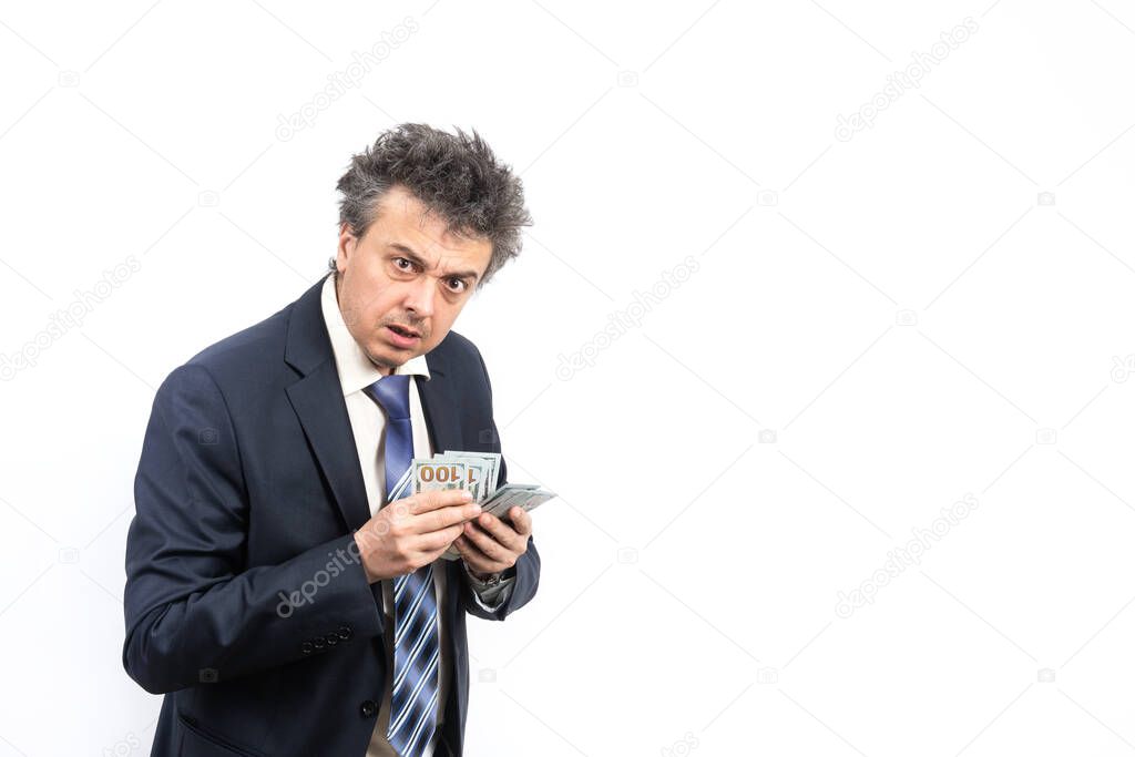 An unshaven middle-aged man in a business suit with disheveled hair and an emotional face holds 100 US dollar bills on a white background