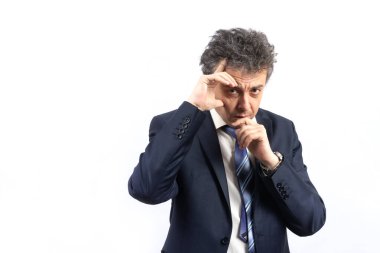 Tıraşsız, orta yaşlı, takım elbiseli, dağınık saçlı ve duygusal bir yüzü olan bir adam beyaz bir arka planda önümüze bakıyor..