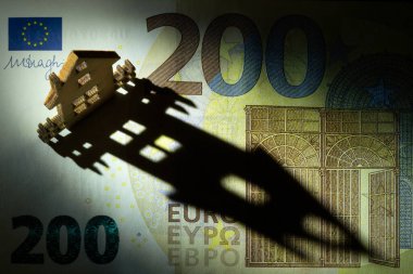 200 avroluk banknotun bir parçasının üzerinde duran küçük, geleneksel ahşap bir ev tasarı alanının üzerine uzun bir gölge düşürüyor..