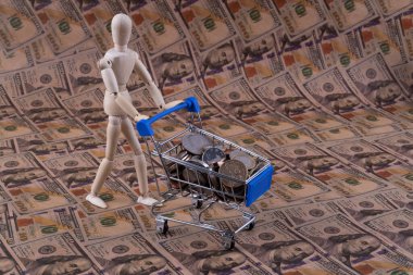 Sembolik bir insan ahşap figürü, 100 dolarlık banknotların arka planında farklı ülkelerin bozuk paralarıyla bir süpermarketten minyatür bir alışveriş arabası taşıyor.