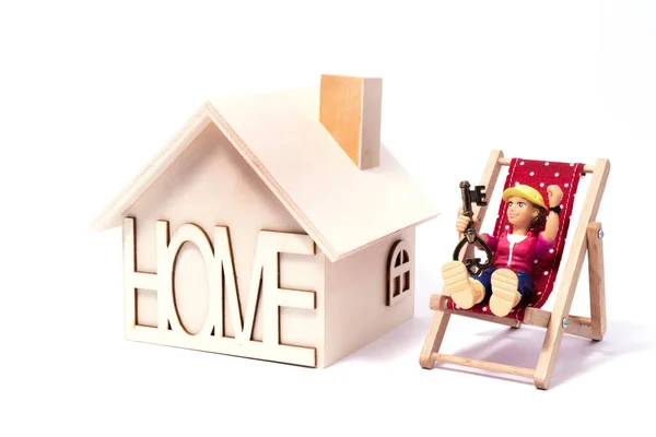 一个右手拿着钥匙的年轻女子的塑料玩具人偶站在一座白色背景的木制象征性房子旁边 — 图库照片