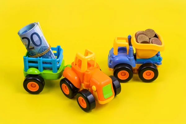 在黄色的背景下 一辆装有欧洲零钱的玩具塑料卡车停在一辆玩具拖拉机旁边 拖车里有20张欧元钞票 — 图库照片