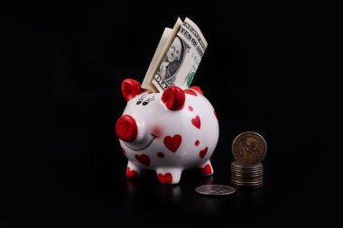 Katlanmış 1 dolarlık banknotları ve siyah arka planı olan komik domuz kumbarası.