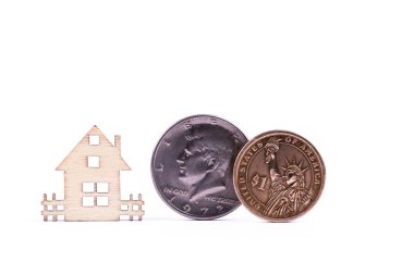 Beyaz arka plandaki ahşap sembolik bir evin yanında 1 dolar ve yarım dolar değerindeki Amerikan sikkeleri.