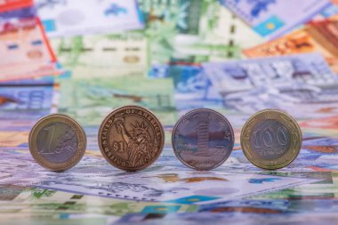 1 Avro, 1 Amerikan Doları, 1 Çin Yuanı ve 100 Kazakistan parasıyla çeşitli mezheplerin arka planında yer alan madeni paralar