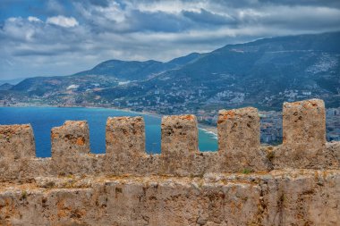 Arka planda bir ortaçağ şatosunun kale duvarı ve Türkiye 'nin Alanya kenti yer alıyor.