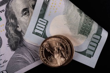 100 dolarlık banknotun arka planına karşılık 1 Amerikan dorllar madeni parası.