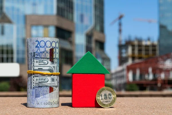 Kazakistan 'da 20.000 tenge banknot ve 100 tenge madeni para modern binaların arka planında sembolik küçük bir evin yanında.