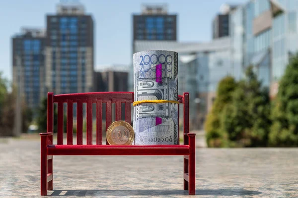 20.000 tenge 'lik Kazakistan banknotları ve modern binaların arka planına karşı sembolik küçük bir bankta 100 tenge' lik bir sikke.