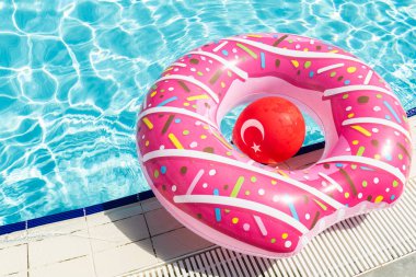 Pembe donut şeklinde şişme çocuk parkı ve kaka içinde suyun üzerinde ulusal Türkiye bayrağı şeklinde kırmızı top.
