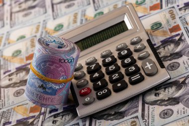 A stack of 10,000 Kazakhstani tenge bills and a calculator for 100 US dollar bills