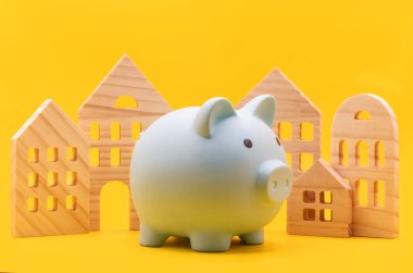 Mavi bir kumbara ve sarı arka planda sembolik ahşap evler.