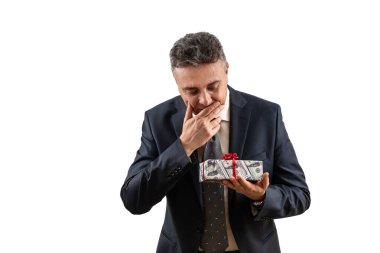 Orta yaşlı takım elbiseli bir adam içinde 100 dolarlık banknotların resmi olan bir hediye kutusu tutuyor..