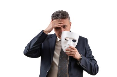 Takım elbiseli orta yaşlı bir adam elinde beyaz bir maske tutuyor.