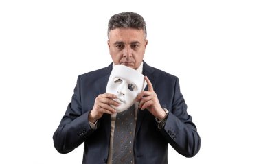 Takım elbiseli orta yaşlı bir adam elinde beyaz bir maske tutuyor.