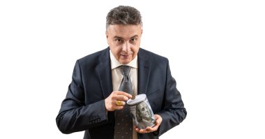 Takım elbiseli orta yaşlı bir adam 1 dolarlık bozuk para ve üzerinde 100 dolarlık banknot resmi olan bir kumbara taşıyor.