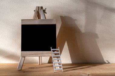 Ahşap tezgahta siyah karatahta ve duvarın arkasında gölgeli bir merdiven.