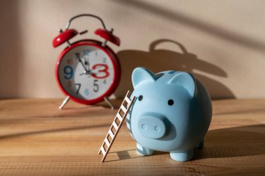 Merdiveni olan bir kumbara ve gölgeli bir duvara dayalı kırmızı bir çalar saat.