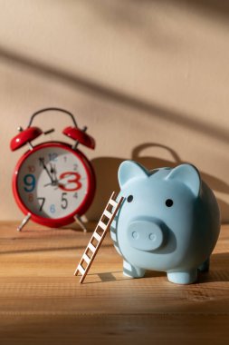 Merdiveni olan bir kumbara ve gölgeli bir duvara dayalı kırmızı bir çalar saat.