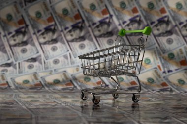 Arkasında 100 dolarlık banknotlar olan boş bir süpermarket arabası.