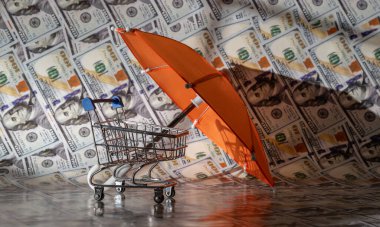 Arka planda 100 dolarlık banknotlarla şemsiyenin altında minyatür bir süpermarket arabası..